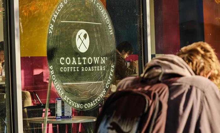 a window with the Coaltown Coffee logo and a man with a bag and coat walking past